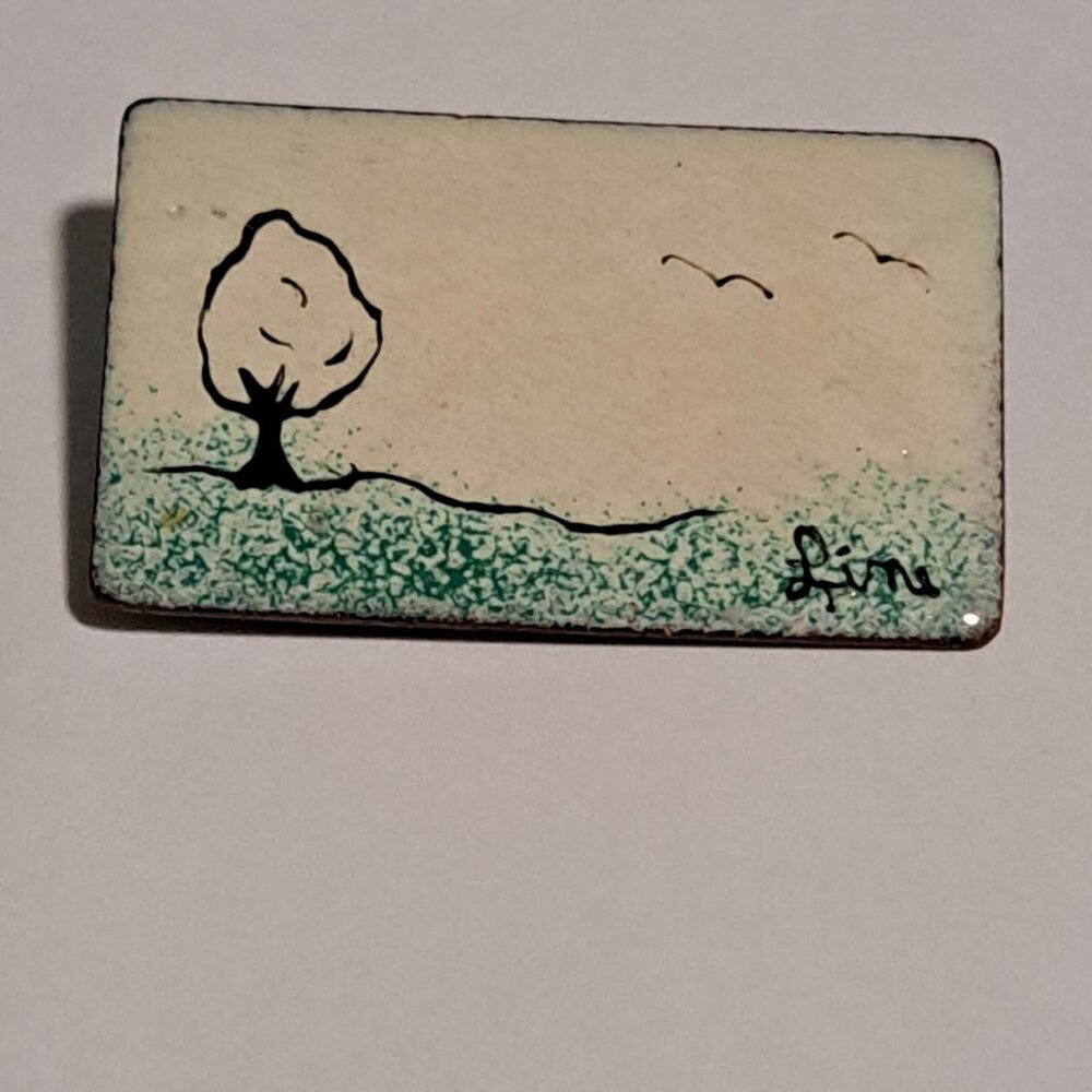Scenic brooch featuring a tree, grass and birds.